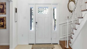 Un pasillo con alfombra estampada, un candelabro, puertas blancas y una escalera con barandilla decorativa.