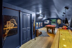 Una habitación con mesa de billar, bolas para jugar al billar, taco y un esqueleto jugando cartas.