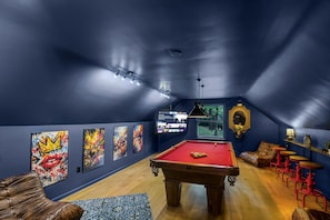 Una mesa de billar en una habitación con paredes azules, obras de arte, un sofá y una pantalla de televisión.