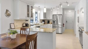 Una cocina moderna con armarios blancos, electrodomésticos de acero inoxidable e iluminación colgante.