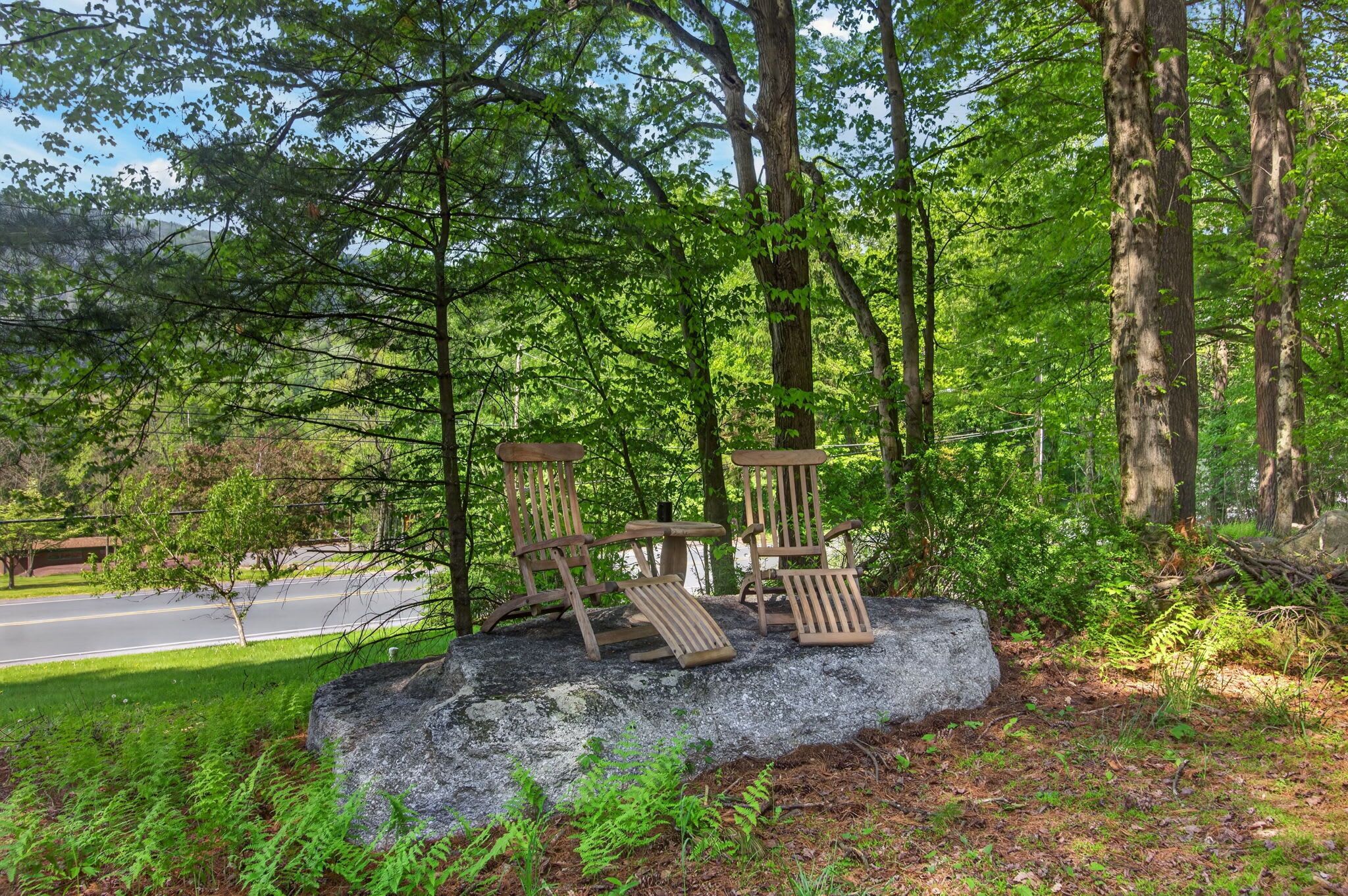 A rock with wooden chairs in a forested area.