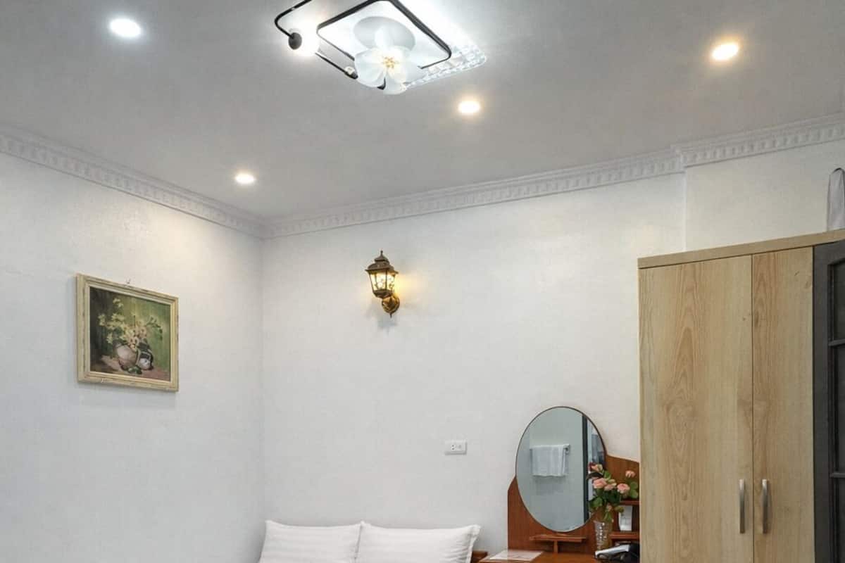 Quarto com cama, guarda-roupa de madeira, escrivaninha com espelho e luminária.
