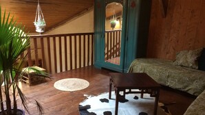 Un'accogliente camera con pavimento in legno, un letto con biancheria a motivi, un tavolino, un tappeto in pelle di mucca, una pianta pensile e un mobiletto blu con uno specchio.