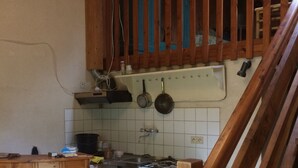 Cucina con mobili in legno, un fornello e pentole appese.