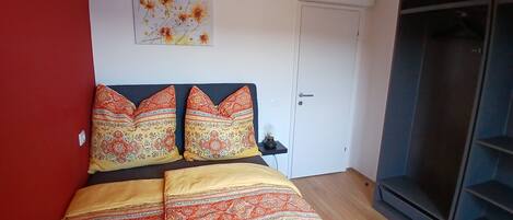 A bedroom with a bed, a red wall, a white door, and a window.