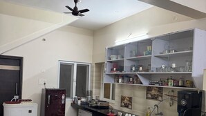 A modern kitchen with a black countertop, a refrigerator, a freezer, and a ceiling fan. - 4BHK Pool Villa In Alibaug- Anushashi's Villa (Alibag)