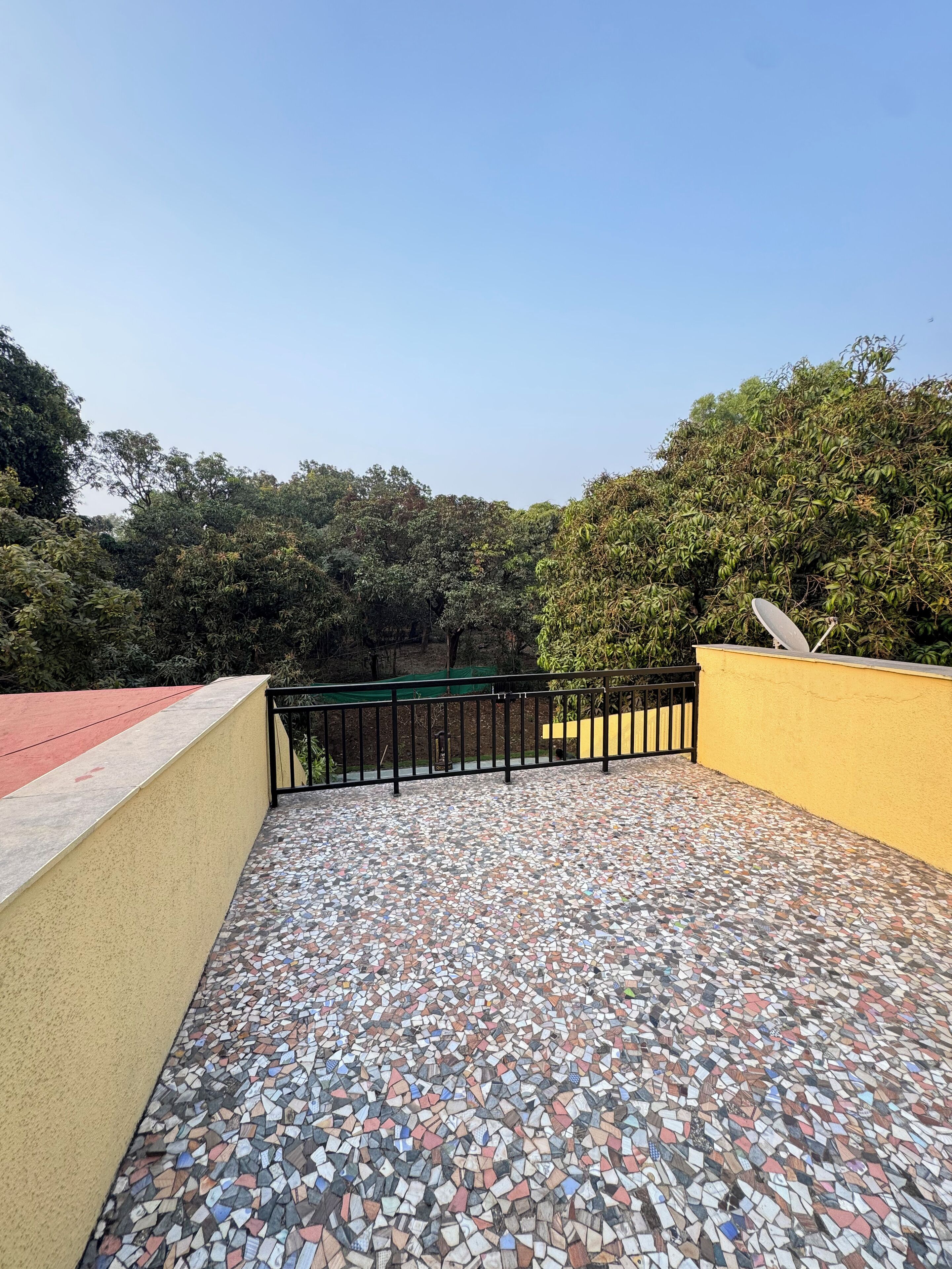 A rooftop terrace with a mosaic floor, surrounded by trees and a yellow wall.
