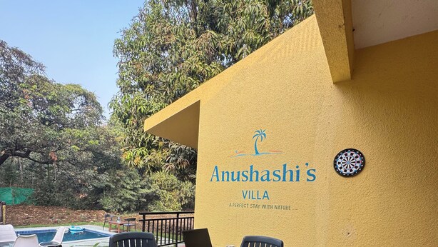 A patio area with a table and chairs, a laptop, and a dartboard at Anushashi's Villa. - 4BHK Pool Villa In Alibaug- Anushashi's Villa (Alibag)