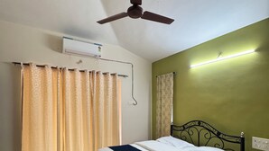 A bedroom with a bed, a ceiling fan, an air conditioning unit, curtains, and a wall-mounted light fixture. - 4BHK Pool Villa In Alibaug- Anushashi's Villa (Alibag)