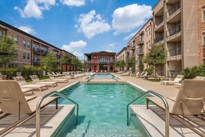 A pool area with lounge chairs and a building with multiple balconies in the background.