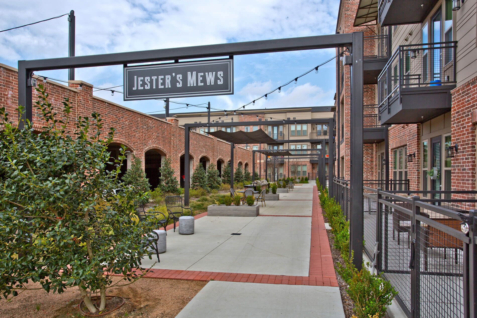 Un patio al aire libre con edificios de ladrillo, asientos exteriores y un letrero que dice "Jester's Mews".