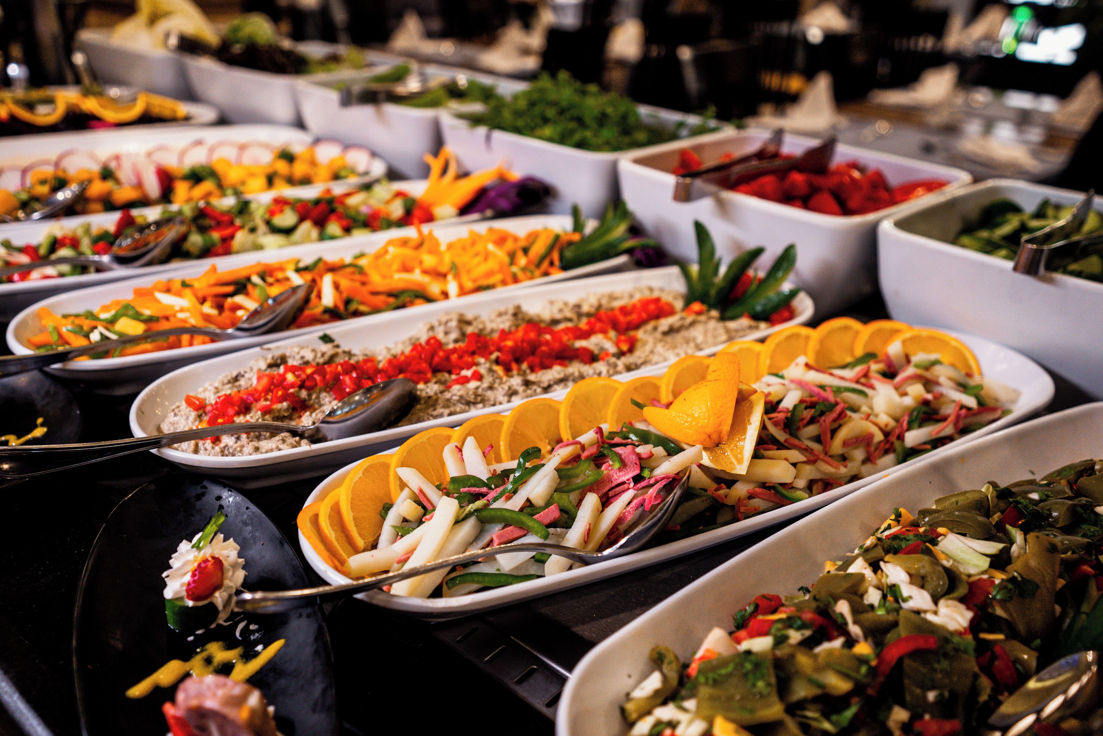 A buffet with various dishes, including salads and fruits, arranged on serving trays.