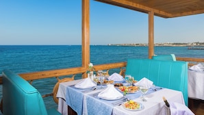 A table set for dining with a view of the sea, wooden beams, and turquoise chairs.