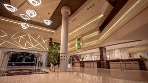 A spacious lobby with a high ceiling, modern lighting fixtures, a central column, and a reception desk.