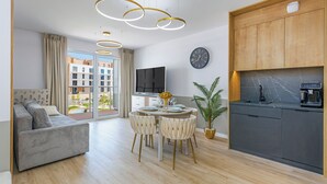 A modern living room with a sofa, dining table, chairs, a TV, and a kitchen area with a coffee machine. - Apartamenty Sun & Snow Bałtyk Jastrzębia Góra (Jastrzębia Góra)