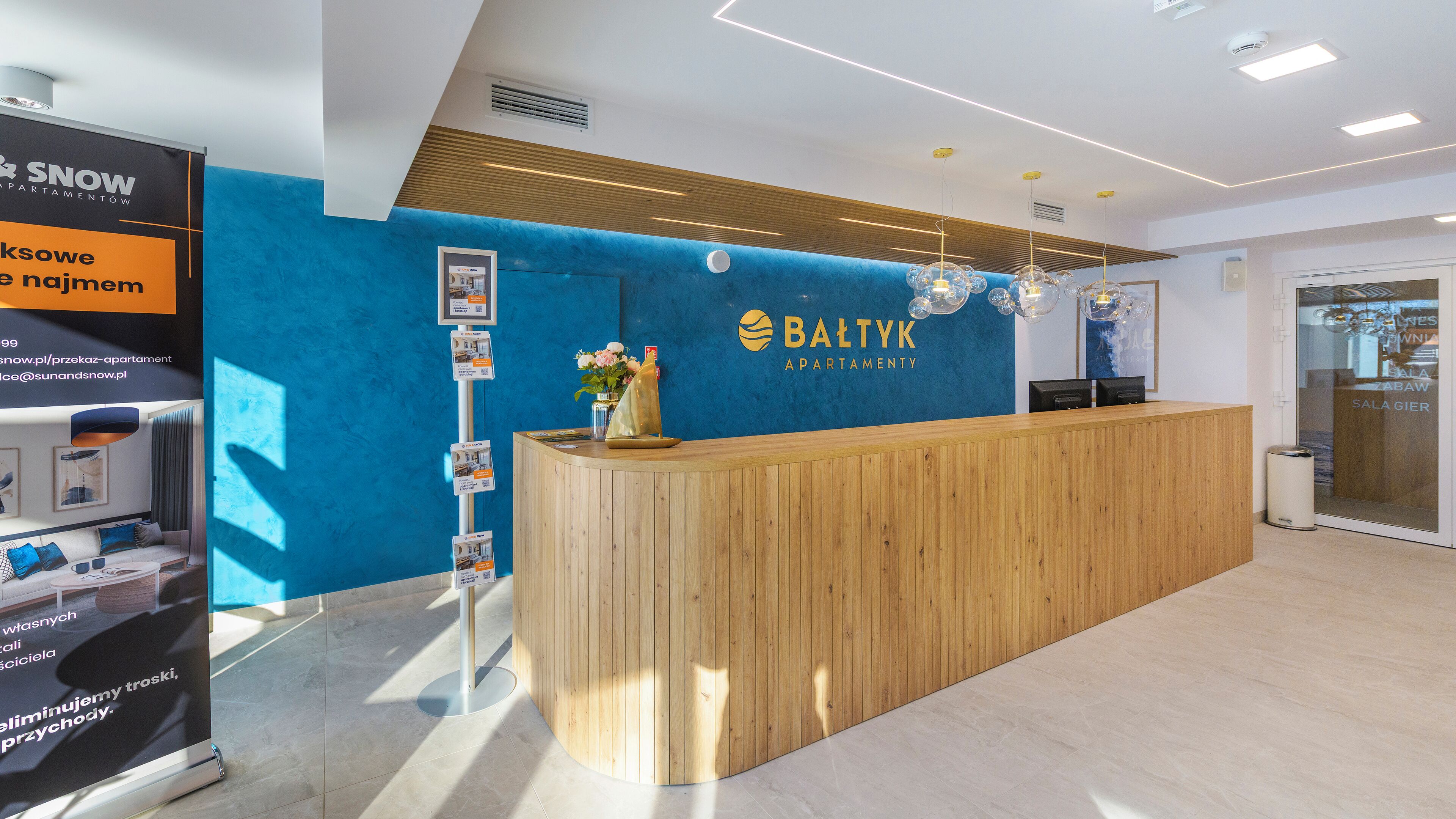 Un área de recepción con un mostrador de madera, una pared de acento azul y un cartel de Baltyk Apartment.
