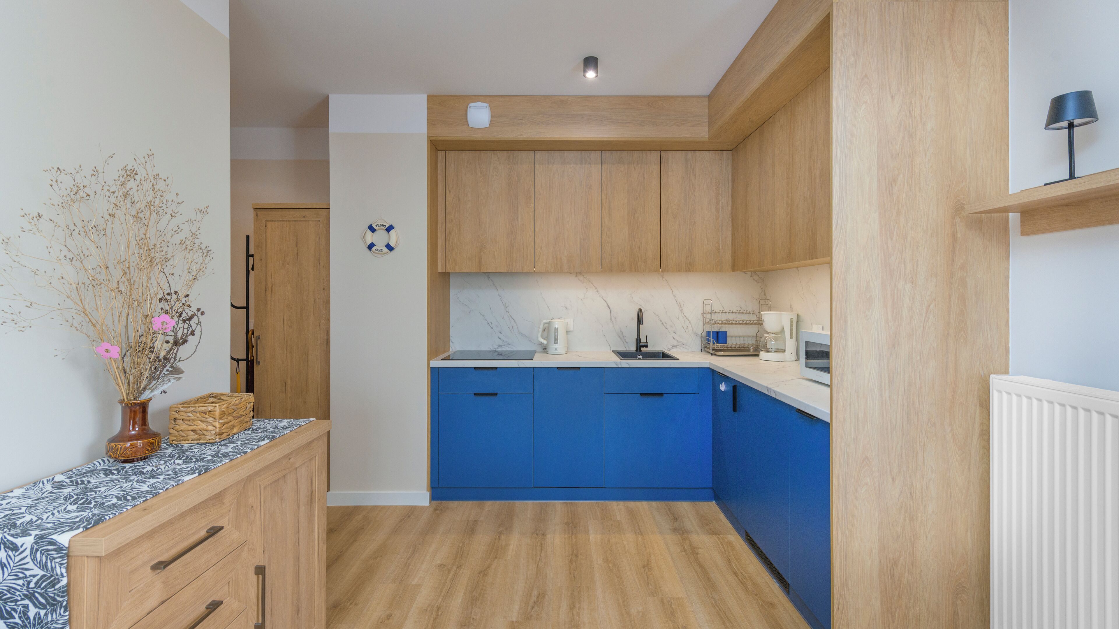 A modern kitchen with blue cabinets, a marble countertop, and a wooden floor.