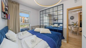 Moderni hotellihuone, jossa on suuri sänky, näkymä kaupungin rakennuksiin, ruokailutila ja kylpyhuone.
