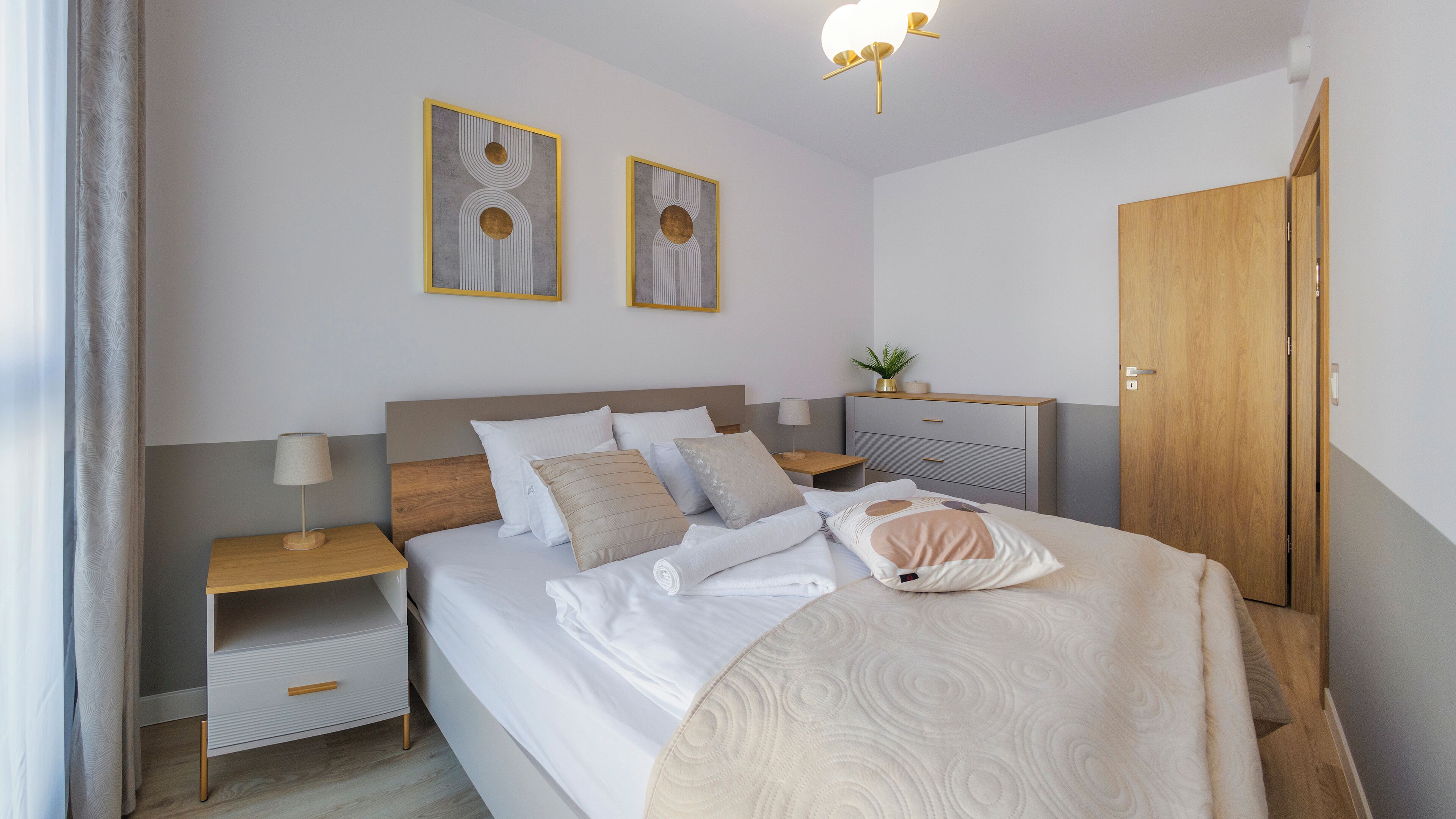 Une chambre à coucher bien rangée, avec un lit, des tables de chevet, une commode, une coiffeuse et deux œuvres d’art encadrées accrochées au mur.