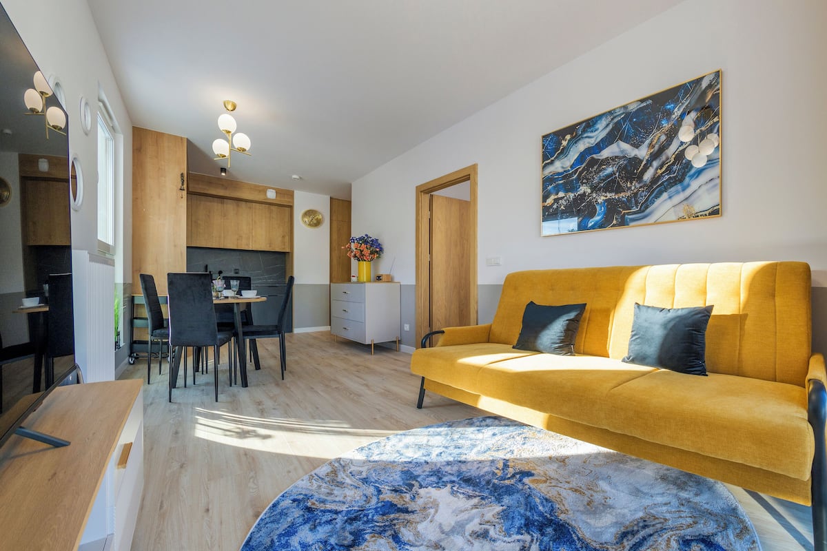 Un salon moderne avec un canapé jaune, un coin repas et une cuisine.