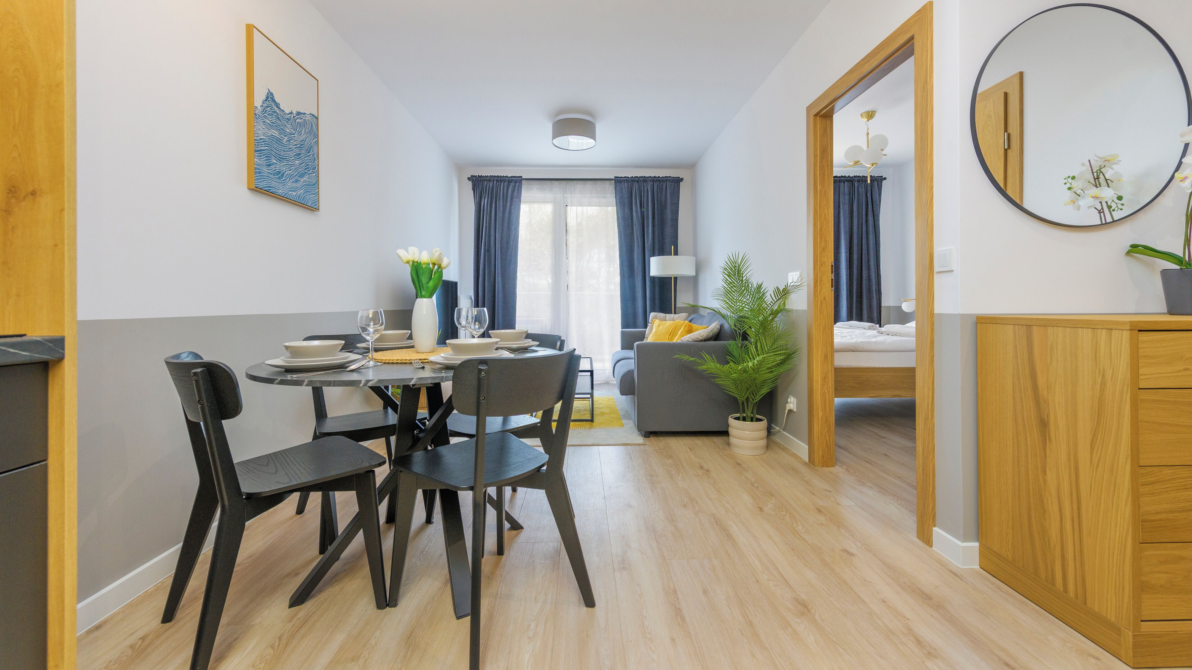 A modern, well-lit room with a dining table, chairs, a sofa, a bed, and a mirror.