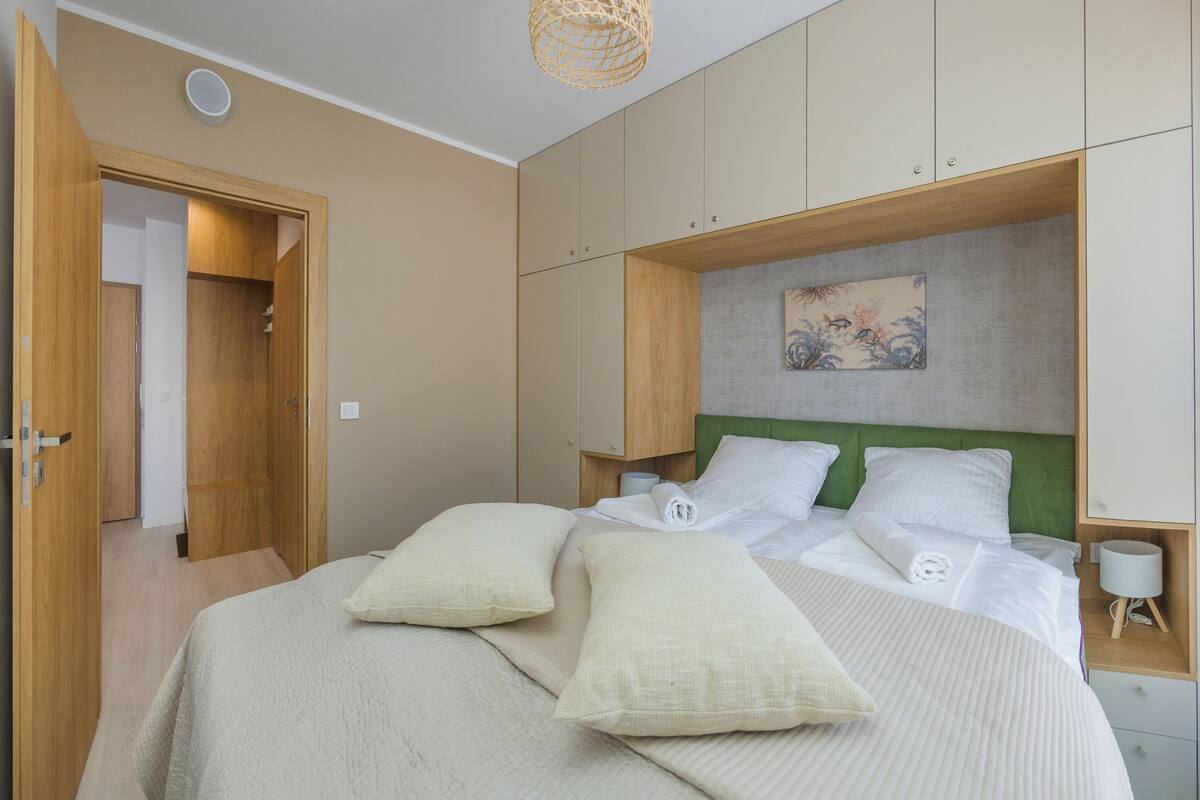 Une chambre à coucher avec un lit, des oreillers, une tête de lit, une table de chevet et une étagère fixée au mur.