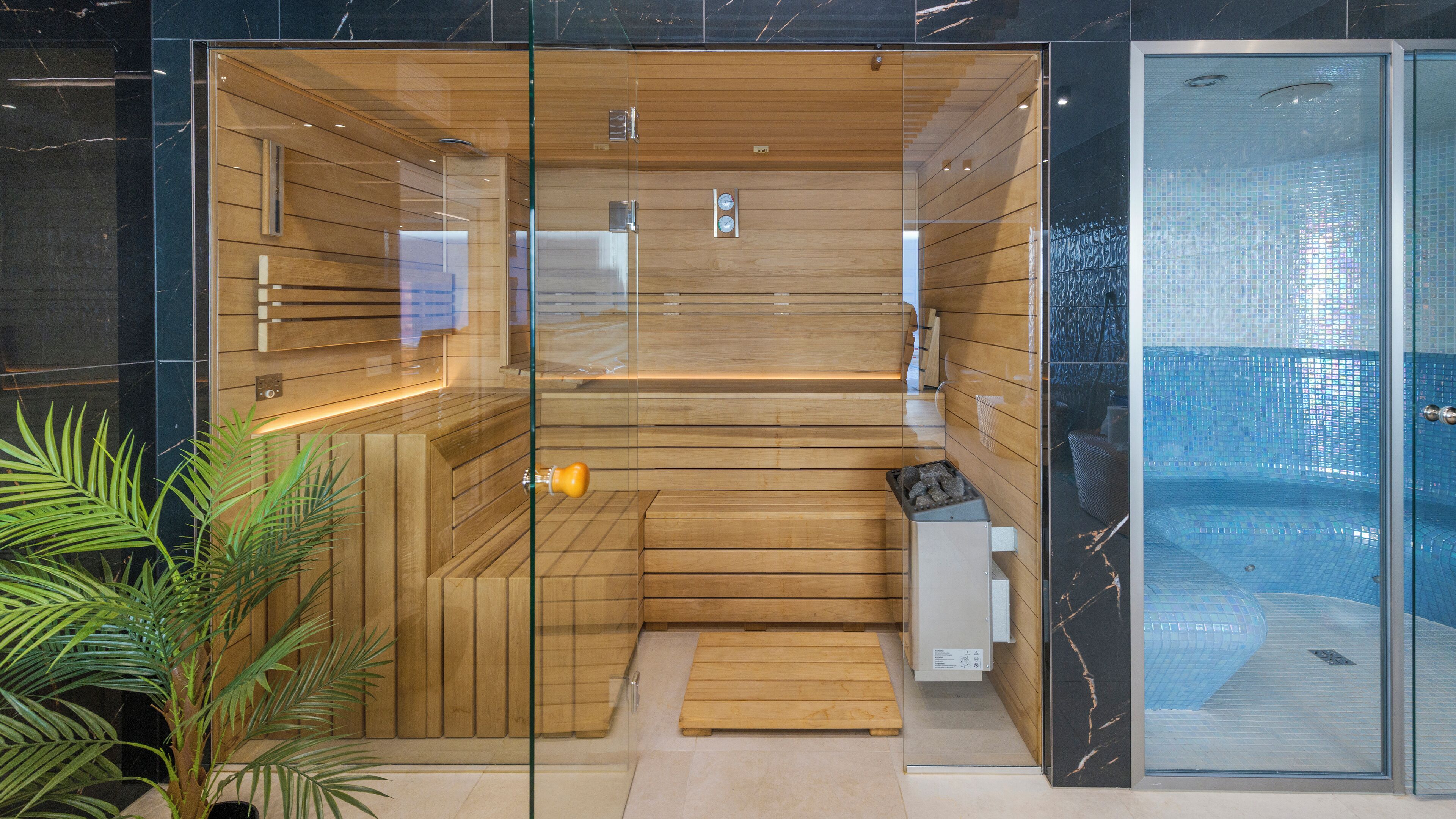 A modern sauna with wooden panels and glass doors, a bench, and a small heater.