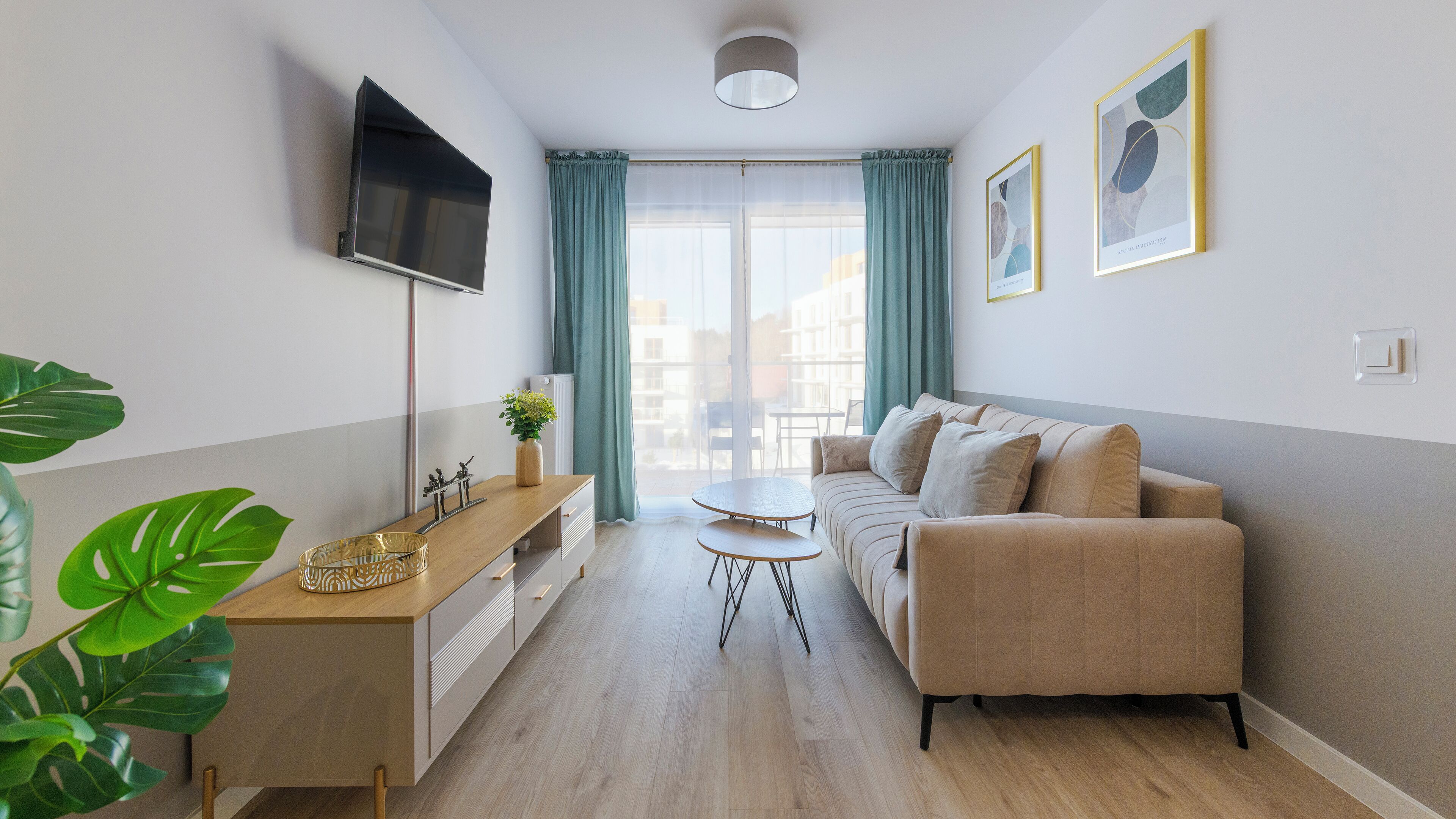 Un salon moderne avec un canapé, un téléviseur fixé au mur, une petite table et une fenêtre avec des rideaux.
