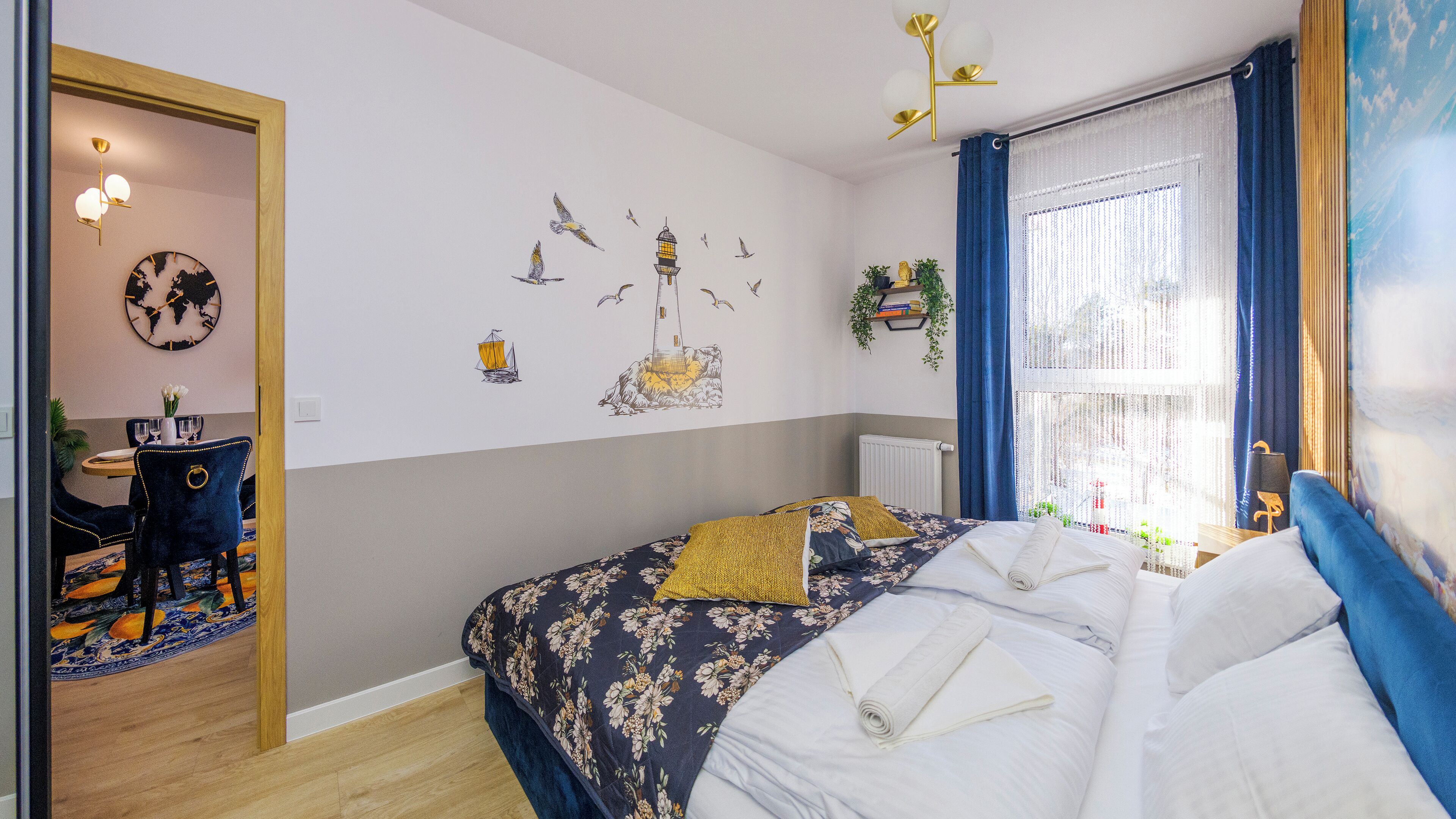 A bedroom with a bed, a desk, and a chair. There is a window with curtains and a view of the outside.