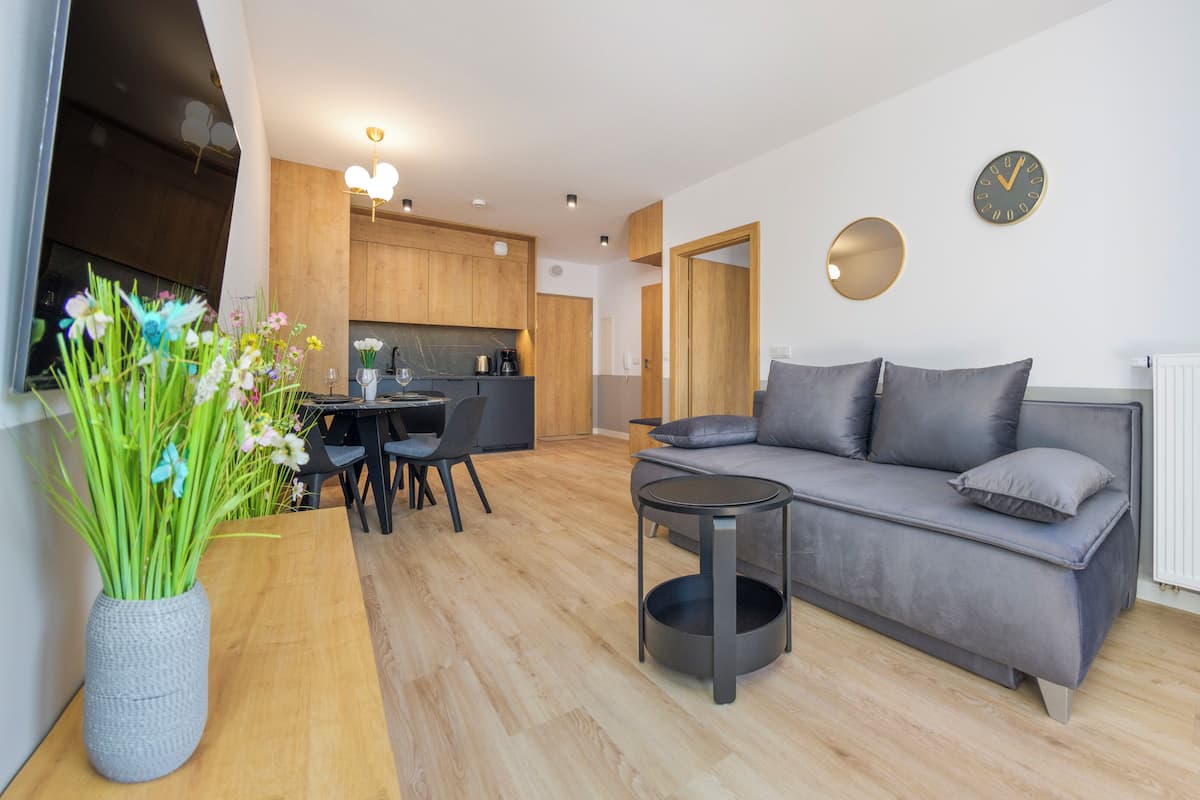 Un salon moderne avec un canapé gris, une petite table ronde et un coin repas comprenant une table et des chaises en bois.