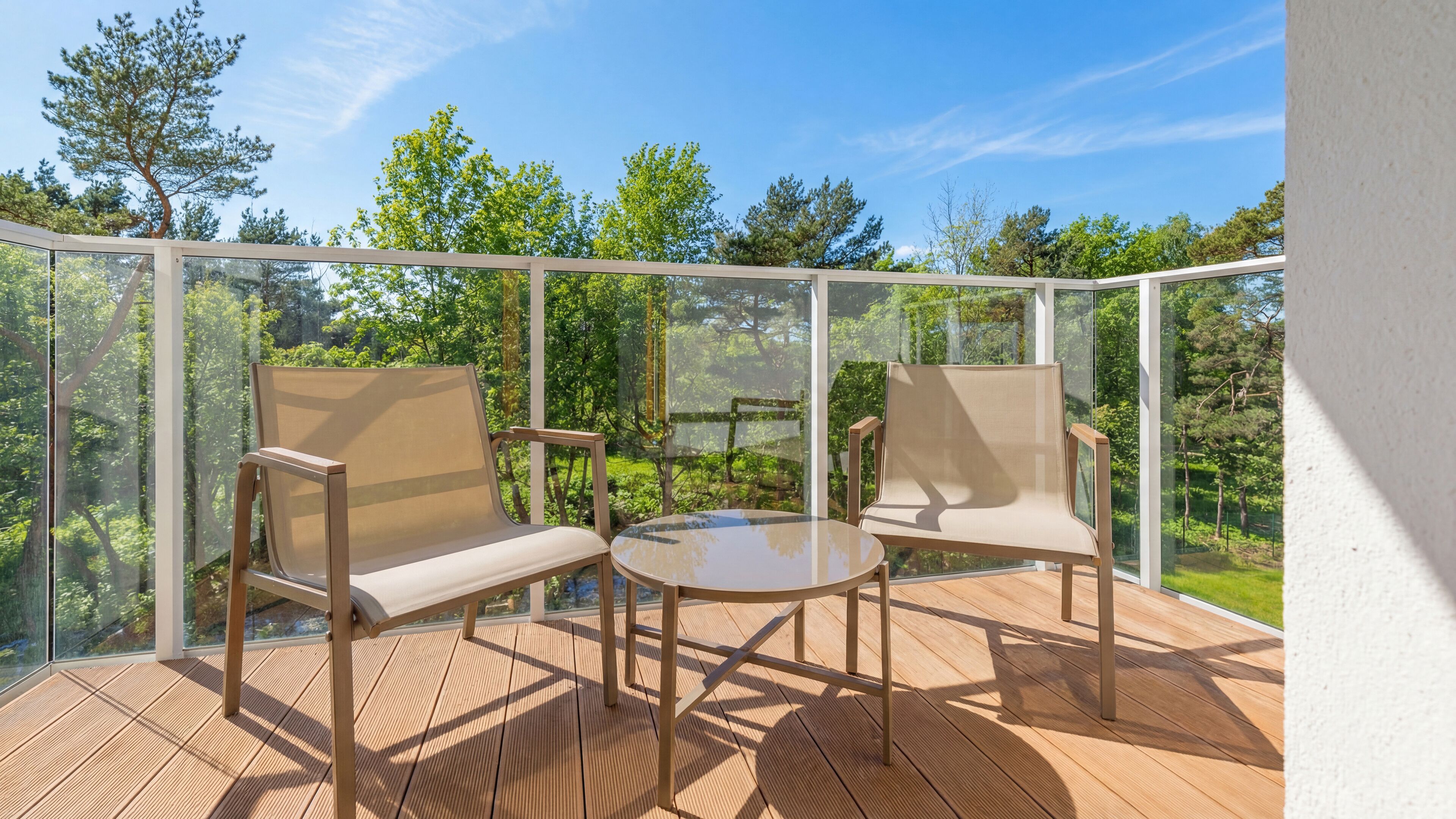 A balcony with two chairs and a table, offering a view of a lush garden and trees.