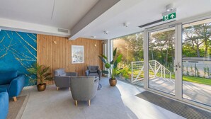 A modern reception area with a blue sofa, two grey armchairs, and a large potted plant. - Apartamenty Sun & Snow Bałtyk Jastrzębia Góra (Jastrzębia Góra)