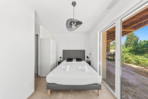Une chambre moderne avec un lit, des tables de chevet et une vue sur l’extérieur, accessible par une porte-fenêtre coulissante.