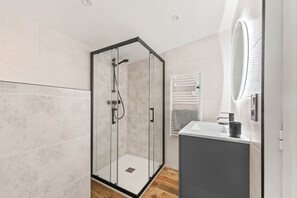 Une salle de bain moderne avec une douche à parois de verre, un lavabo blanc et un miroir.