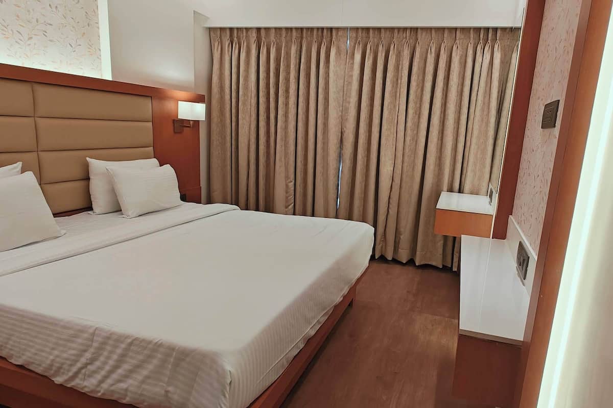 Una habitación de hotel con una cama grande, cabecera, mesita de noche, lámpara y cortina.