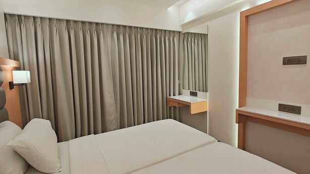 A hotel room with a bed, a nightstand, a mirror, and a window with curtains. - CIESTA SERENE (Navi Mumbai)
