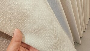 A hand holding a fabric with a textured pattern, likely a curtain or drape, in a store with similar items in the background. - CIESTA SERENE (Navi Mumbai)