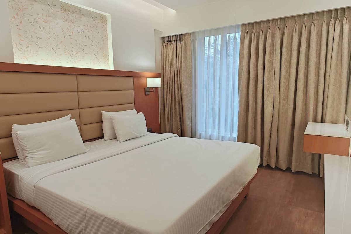 Habitación de hotel con una cama grande, cabecera de madera, dos mesitas de noche y una mesita auxiliar.