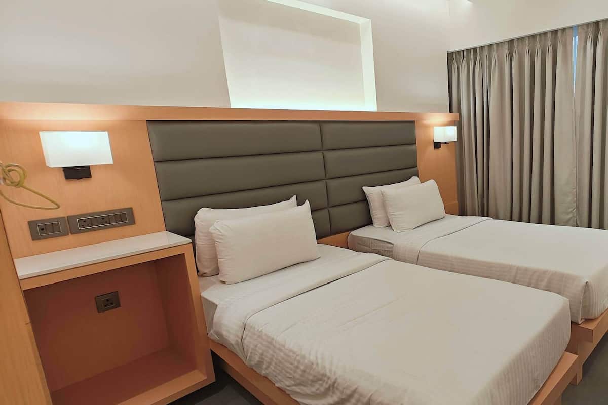 Habitación de hotel con dos camas, televisión, escritorio y ventana con cortinas.