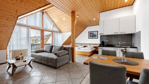 Loft moderno con zona pranzo, cucina e soggiorno, caratterizzato da ampie finestre e soffitto in legno.