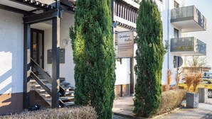 Un edificio con un cartello che riporta 'Gärtner Noller', una scala e due alti alberi sempreverdi.