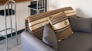 Eine moderne Küche mit Barbereich, ein graues Sofa mit gemusterten Kissen und ein Gemälde einer Kirche an der Wand.