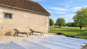 Eine Terrasse mit zwei Liegestühlen und einem überdachten Bereich, neben einem Steinhaus mit Ziegeldach.