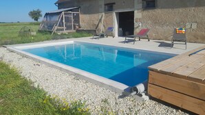 Ein Schwimmbecken mit klarem, blauem Wasser, umgeben von einer Kiesfläche, und im Hintergrund ein Gebäude mit einem Ziegeldach.