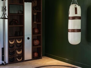 A room with a punching bag, a cabinet with leather items, and a metal object on the floor.