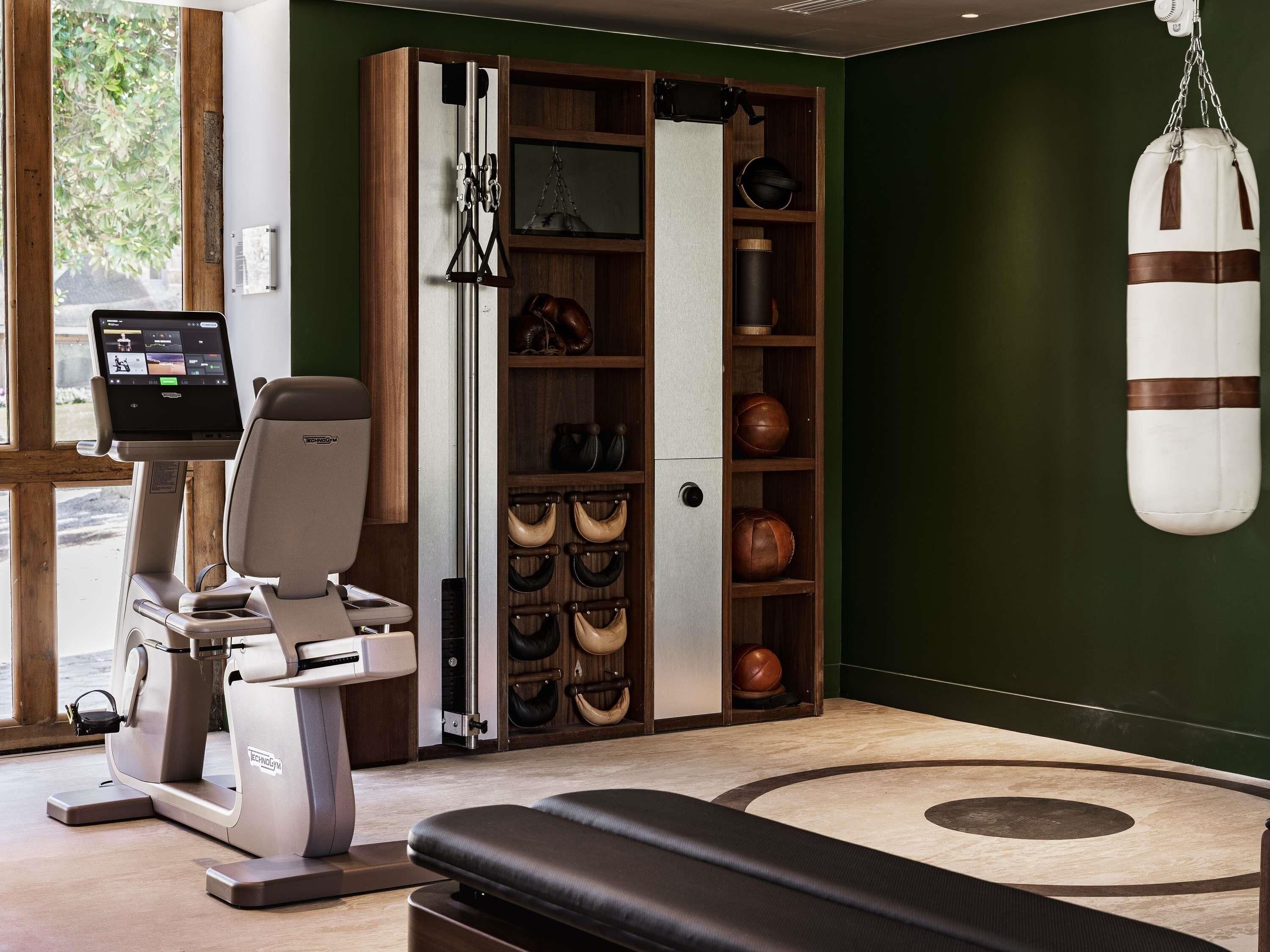 Una sala de fitness amb cinta de córrer, sac de boxa i pantalla penjada a la paret.