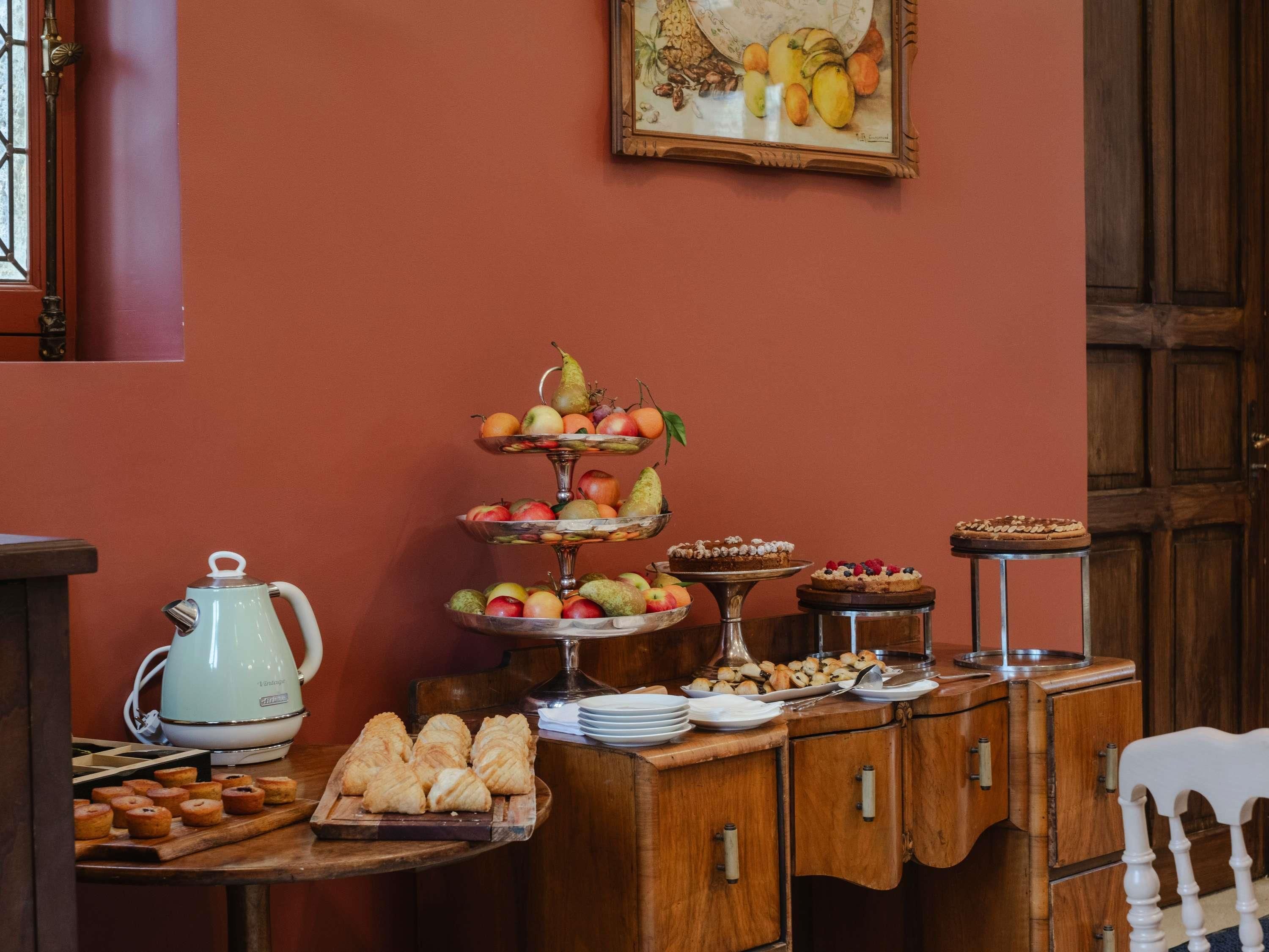 Een buffetopstelling met een fruitplateau, een waterkoker, gebak en een schilderij aan de muur.