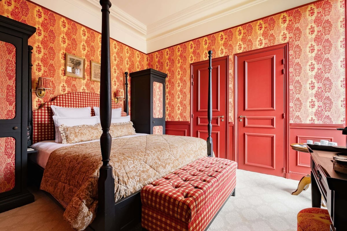 A four-poster bed with a checkered bench, a wardrobe, and a desk with a lamp.