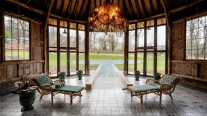A rustic wooden room with a high ceiling, large windows, wicker furniture, and a central pathway leading to an outdoor area.
