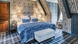 Un dormitorio con una cama, dos mesitas de noche, un banco y papel tapiz estampado.